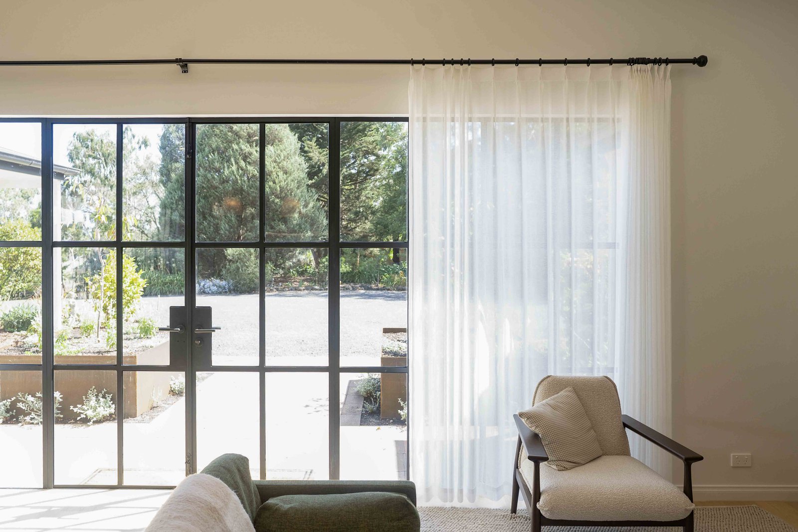Living room with large black-framed glass doors, sheer white curtains.