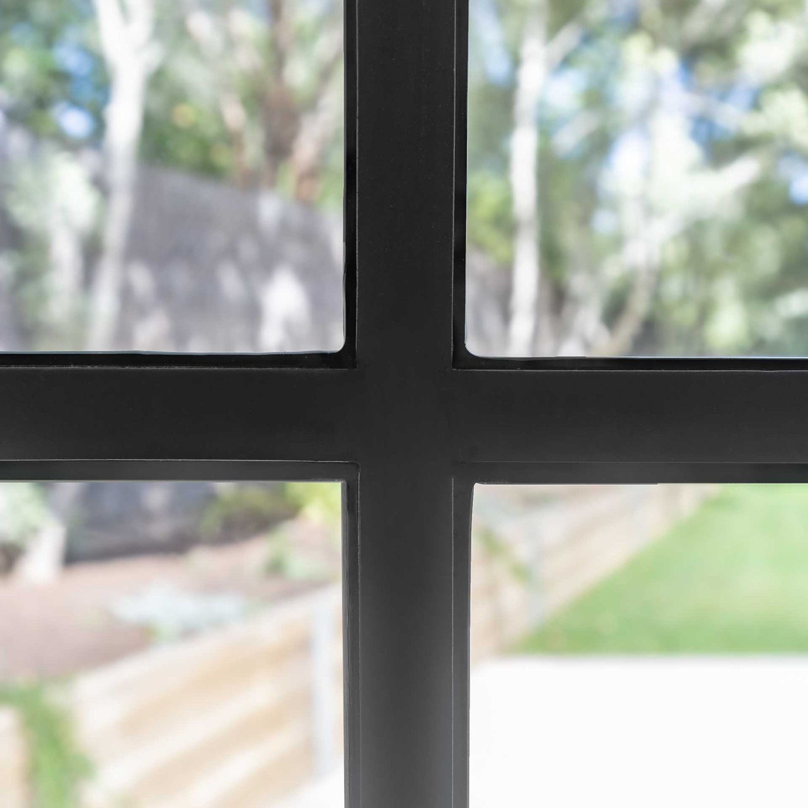 Close-up of black metal window frame with a blurred view of an outdoor garden and fence.